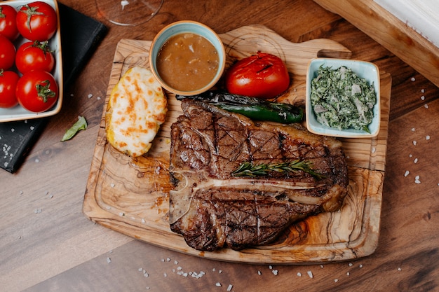 Draufsicht auf gegrilltes Rindersteak, serviert mit Gemüse und Soße auf einem Holzbrett