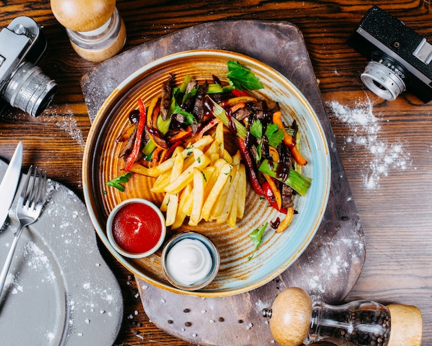 Draufsicht auf gegrilltes rindfleisch mit gemüse, das mit pommes frites und saucen auf einem teller serviert wird