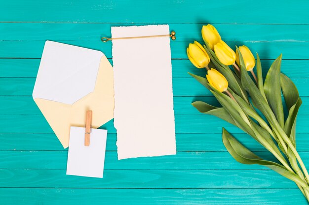 Draufsicht auf gelbe Tulpenblumen; leeres Blatt; und öffnen Sie den Umschlag über dem grünen Hintergrund