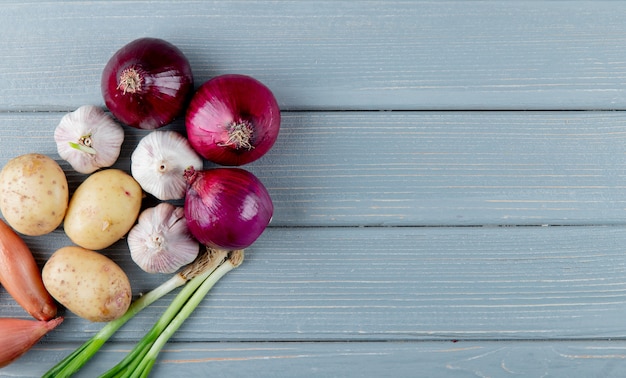 Draufsicht auf Gemüse als Kartoffel-Knoblauch-Schalotte und Zwiebel auf der linken Seite und hölzernem Hintergrund mit Kopienraum