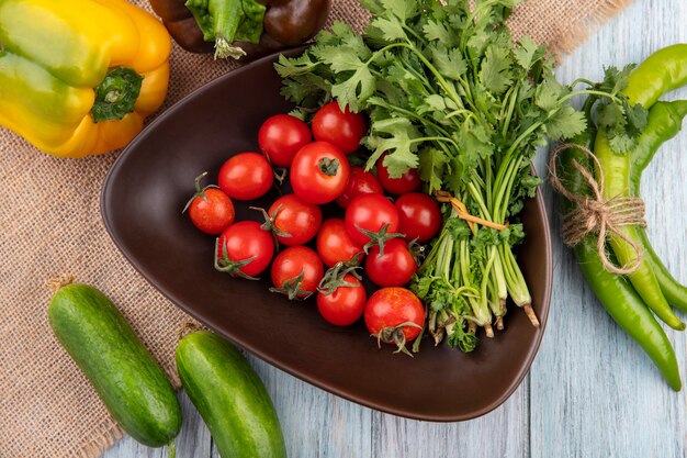 Draufsicht auf Gemüse als Tomatenbündel Koriander in Schüssel mit Paprika auf Sackleinen und auf Holzoberfläche