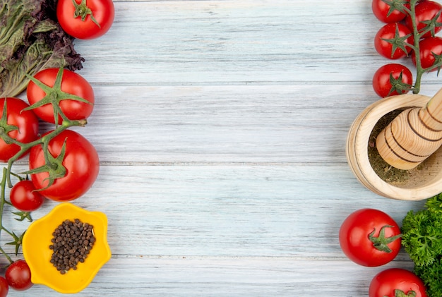 Draufsicht auf Gemüse als Tomatenkoriander mit Knoblauchbrecher mit schwarzem Pfeffer auf der linken und rechten Seite und Holzoberfläche mit Kopierraum