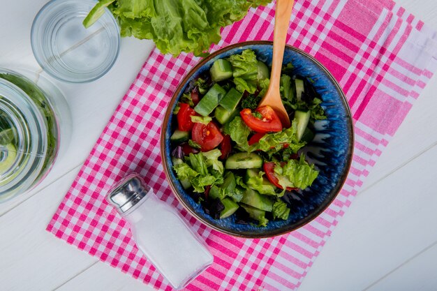 Draufsicht auf Gemüsesalat und Salz auf kariertem Stoff mit Entgiftungswasser und Salat auf Holz