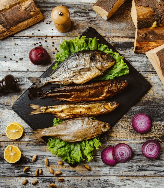 Draufsicht auf geräucherten Fisch, der mit Salat auf schwarzem Servierbrett serviert wird