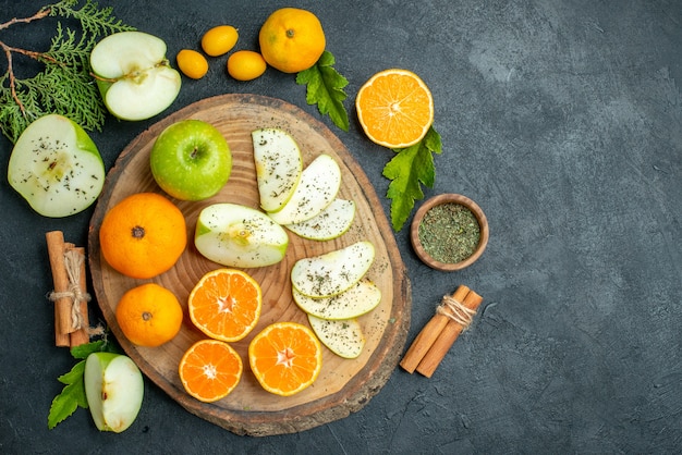 Draufsicht auf geschnittene Äpfel und Mandarinen auf rustikalem Servierbrett Zitronenscheiben getrocknetes Minzpulver auf dunklem Tisch