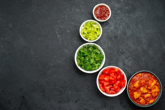 Draufsicht auf geschnittene rote Tomaten mit Grün auf Grau