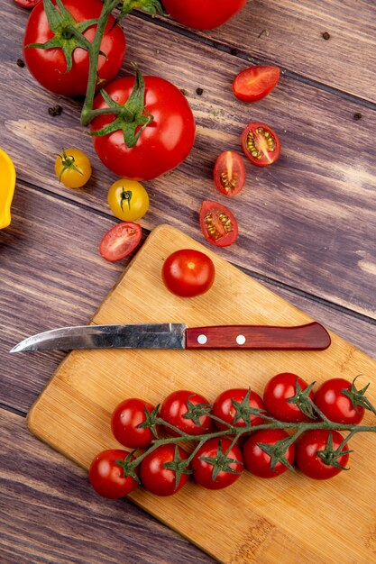 Draufsicht auf geschnittene und ganze Tomaten mit Messer auf Schneidebrett auf Holz