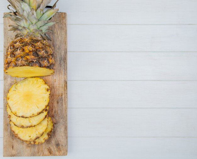 Draufsicht auf geschnittene und geschnittene Ananas auf Schneidebrett auf der linken Seite und hölzernem Hintergrund mit Kopienraum