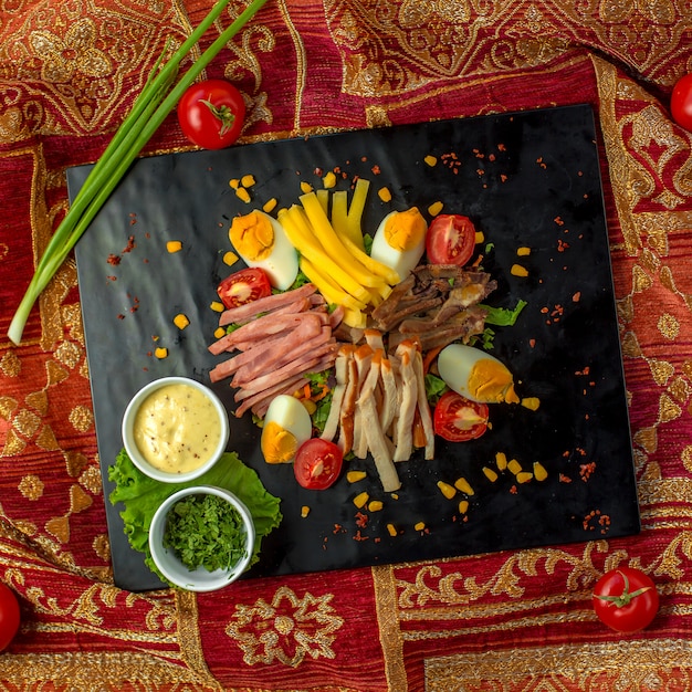 Draufsicht auf geschnittenen Schinken serviert mit Eiern Tomaten und Saucen auf einer schwarzen Tafel