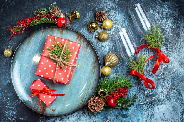 Draufsicht auf Glasbecher mit roten Geschenkboxen auf blauem Teller und Dekorationszubehör aus Tannenzweigen auf dunklem Hintergrund