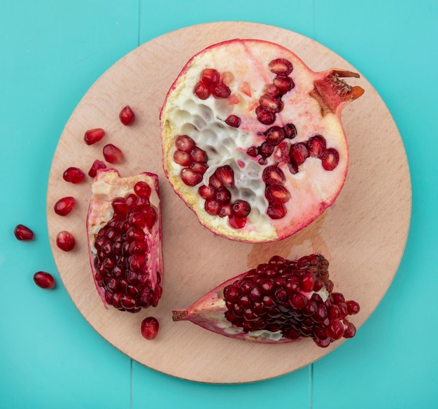 Draufsicht auf Granatapfelstücke und Granatapfelhälfte mit Beeren auf Schneidebrett auf blauer Oberfläche