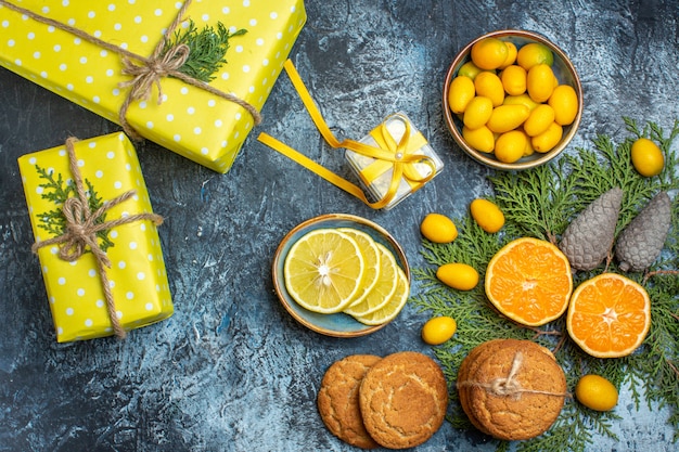 Draufsicht auf halbe und ganze frische zitrusfrüchte und gelbe geschenkbox-nadelkegel köstliche kekse auf dunklem hintergrund Kostenlose Fotos