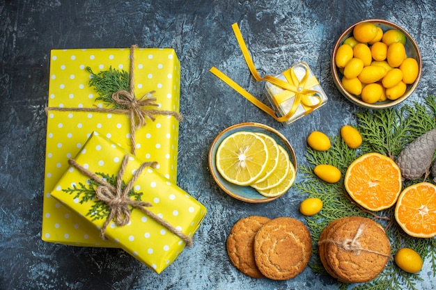 Kostenloses Foto draufsicht auf halbe und ganze frische zitrusfrüchte und gelbe geschenkbox-nadelkegel köstliche kekse auf dunklem hintergrund