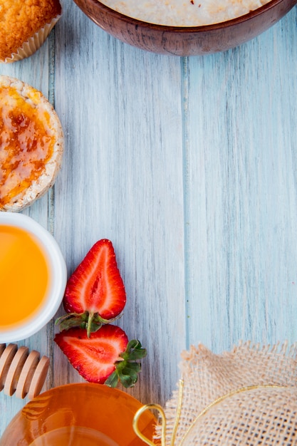 Kostenloses Foto draufsicht auf halbgeschnittene erdbeeren mit hafer-knäckebrot-pfirsichsirup-cupcake-butter auf holzoberfläche mit kopierraum