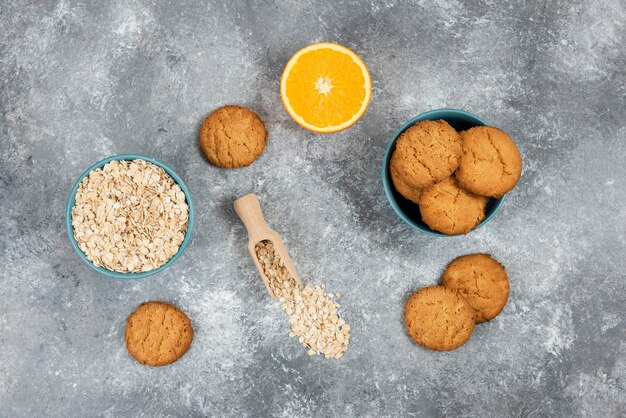 Draufsicht auf hausgemachte Kekse auf Holzbrett und Haferflocken mit Orangen.