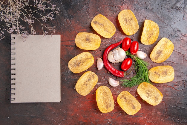 Kostenloses Foto draufsicht auf hausgemachte köstliche knusprige chips rote paprika knoblauch grüne tomaten und notebook auf dunklem tisch