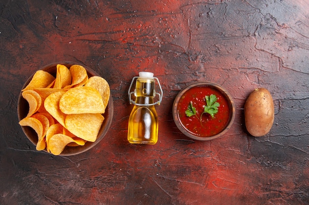 Draufsicht auf hausgemachte köstliche knusprige Kartoffelchips in einem braunen Topf gefallene Ölflasche Ketchup-Tomatenkartoffel auf dunklem Hintergrund