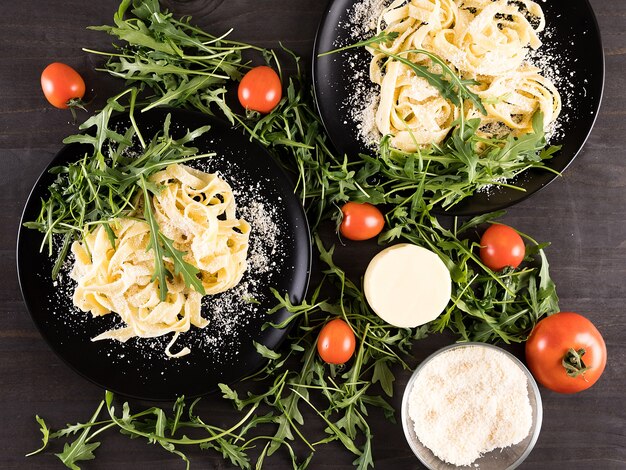 Draufsicht auf hausgemachte Tagliatelle-Nudeln mit Parmesan, Kirschtomaten und Grün