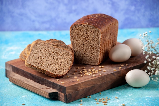 Draufsicht auf in Hälften geschnittene Schwarzbrotscheiben auf Holzbrettern Blumeneier auf hellem eisblauem Hintergrund