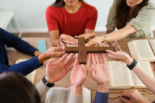 Draufsicht auf junge Frauen und Männer, die Teil einer religiösen Gruppe sind, die ein katholisches Kreuz zusammenhalten und beten