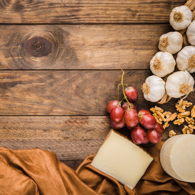 Draufsicht auf Käse; rote Trauben; Walnuss und Knoblauch über Holztisch