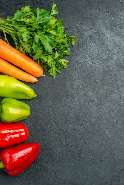 Draufsicht auf Karottengrün und Paprika auf der linken Seite auf dem dunkelgrauen Tisch