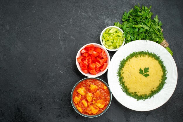 Draufsicht auf Kartoffelpüree mit Grüns und Tomatenscheiben auf Grau