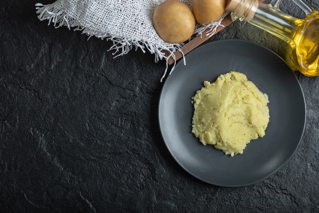 Draufsicht auf Kartoffelpüree und frische Kartoffeln. Kartoffelpüree auf schwarzem Teller.