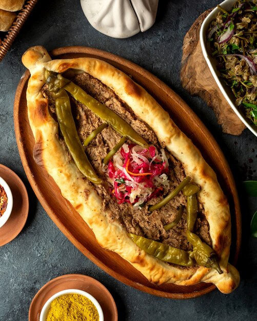 Draufsicht auf Khachapuri der traditionellen georgischen Küche mit Fleisch und eingelegtem heißem Chili-grünem Pfeffer in einer Holzplatte