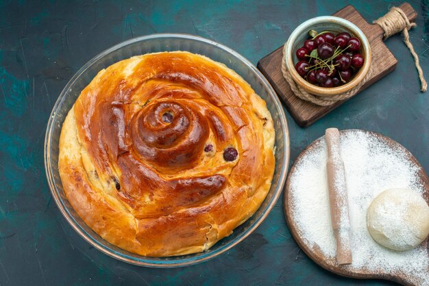 Draufsicht auf Kirschkuchen mit Teigmehl und frischen Sauerkirschen auf dunkelblauen süßen Tortenkuchenkuchenfrüchten