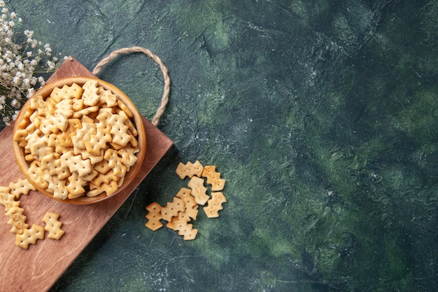 Draufsicht auf kleine gesalzene Cracker in Schüssel auf Holzbrett