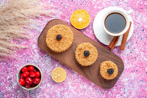 Draufsicht auf kleine köstliche Kuchen rund gebildet mit Zimt und Tee auf der hellrosa Oberfläche