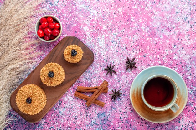 Draufsicht auf kleine köstliche Kuchen rund mit Zimt und Tee auf der rosa Oberfläche gebildet