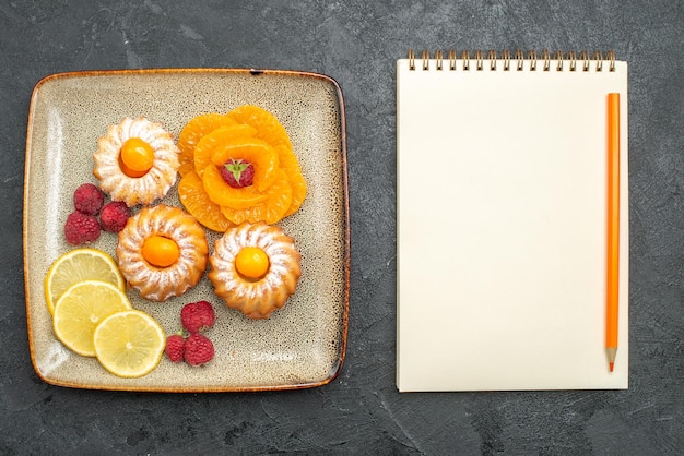 Draufsicht auf kleine leckere Kuchen mit geschnittenen Zitronenmandarinen auf Grau