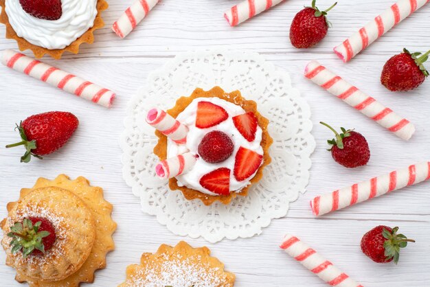 Draufsicht auf kleine leckere Kuchen mit Sahne und geschnittenen Erdbeersüßigkeiten auf Weiß