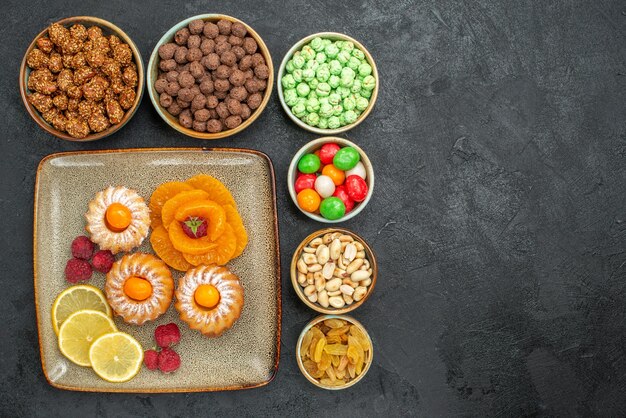 Draufsicht auf kleine leckere Kuchen mit Zitronenscheiben, Mandarinen und Bonbons auf Grau