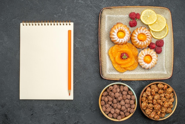 Draufsicht auf kleine leckere Kuchen mit Zitronenscheiben, Mandarinen und Bonbons auf Grau