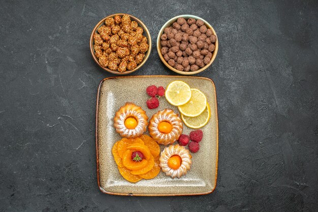 Draufsicht auf kleine leckere Kuchen mit Zitronenscheiben, Mandarinen und Bonbons auf Grau