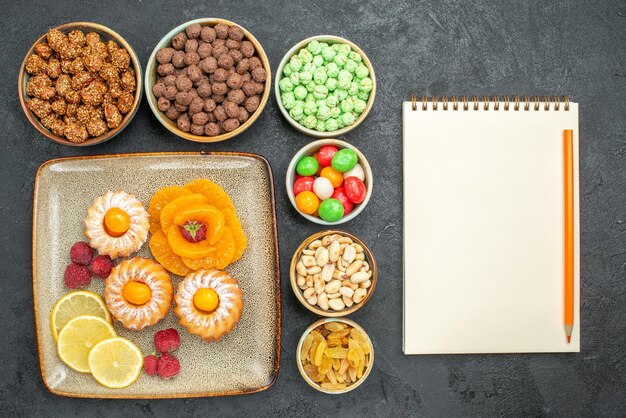 Draufsicht auf kleine leckere Kuchen mit Zitronenscheiben, Mandarinen und Bonbons auf Grau