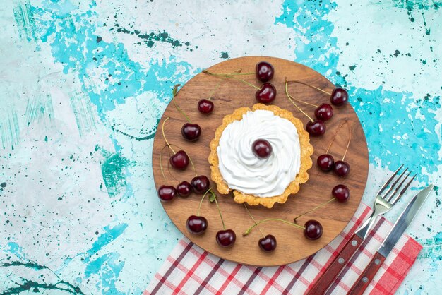 Draufsicht auf kleinen Kuchen mit Sahne und Frischkirschen auf hellblauem, fruchtfrischem Kuchenkeks süß