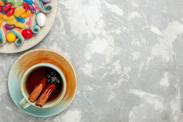 Draufsicht auf köstliche bunte Bonbons mit Marmelade und Tasse Tee auf weißer Oberfläche