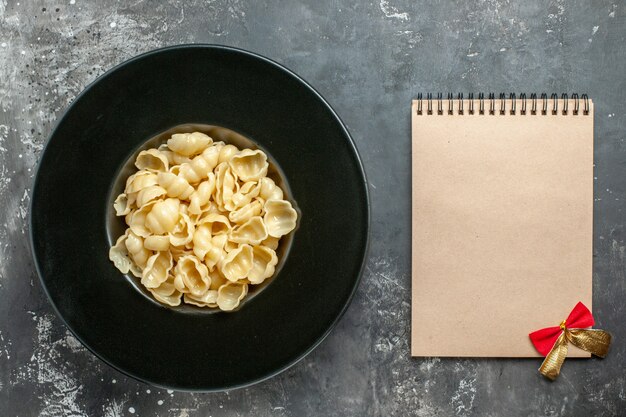 Draufsicht auf köstliche Conchiglie auf schwarzem Teller und Notizbuch auf grauem Hintergrund