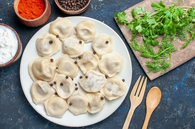 Draufsicht auf köstliche gebackene Knödel innerhalb Platte zusammen mit Pfeffer und Grün auf dunklem Boden, Mahlzeit Essen Abendessen Fleischkalorie