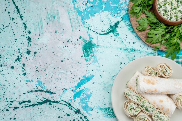 Draufsicht auf köstliche Gemüsebrötchen ganz und in Scheiben geschnitten mit Gemüse und Salat auf hellblauem Schreibtisch, Gemüsesnack mit Speisenmahlzeit