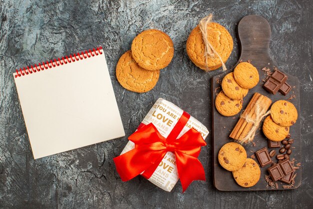 Draufsicht auf köstliche Keks-Schokoriegel und Geschenkbox-Spiralnotizbuch auf eisiger dunkler Oberfläche