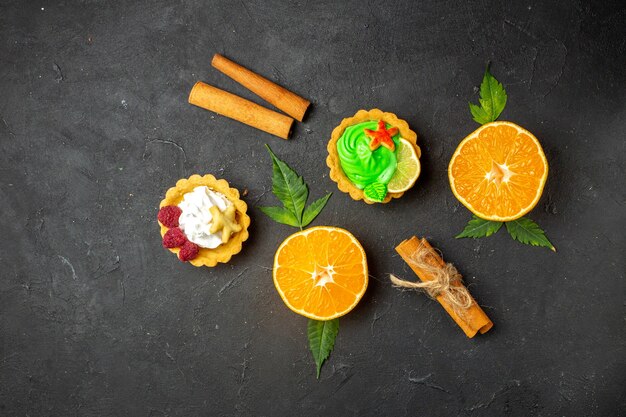 Draufsicht auf köstliche Kekse, Zimtlimetten und halbgeschnittene Orangen mit Blättern auf dunklem Hintergrund