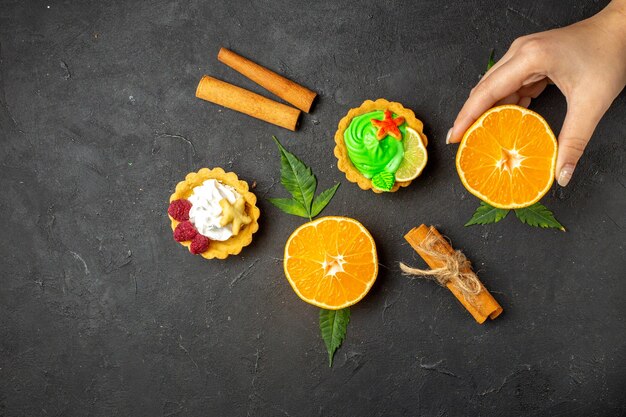 Draufsicht auf köstliche Kekse, Zimtlimetten und halbgeschnittene Orangen mit Blättern auf dunklem Hintergrund