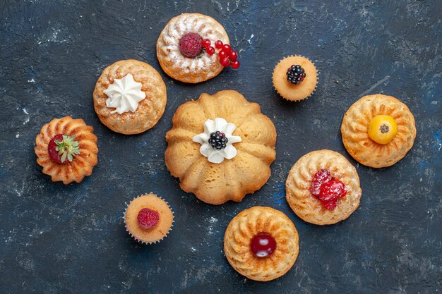 Draufsicht auf köstliche Kuchen, die mit Sahne und Beeren auf dunklem Schreibtisch gebacken werden, Beerenfruchtkuchenkeks süß