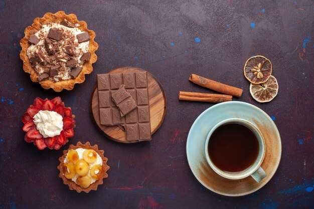 Draufsicht auf köstliche Kuchen mit Sahne-Schokolade und Früchten zusammen mit Tee auf der dunklen Oberfläche