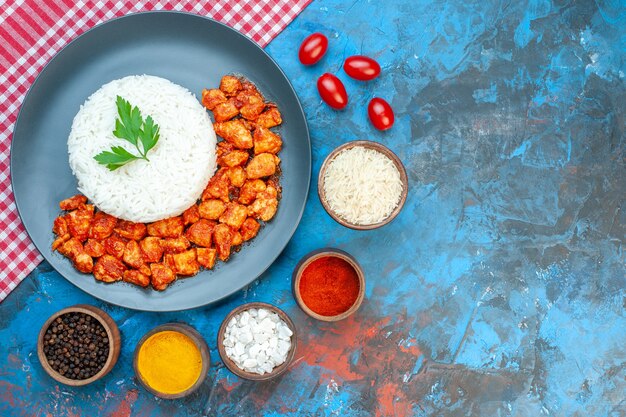 Draufsicht auf köstliche Reisgerichte mit grünem und tomatigem Hühnchen auf rotem, abgestreiftem Handtuch verschiedene Gewürze Tomaten auf blauem Tisch